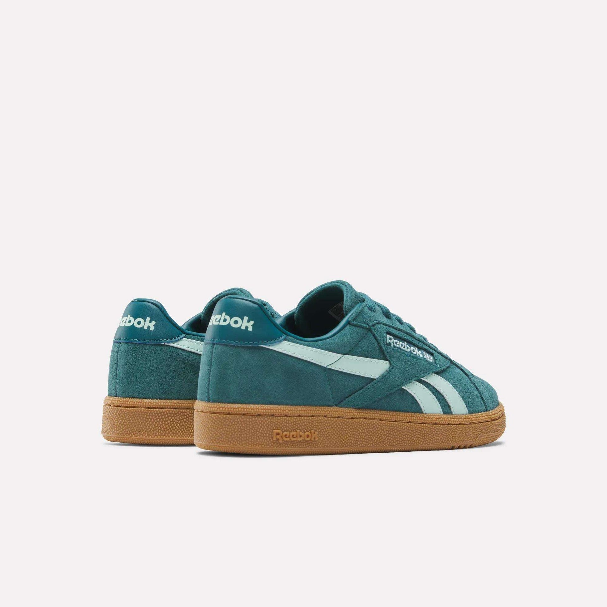 The Women's Club C Grounds UK Shoes by Reebok feature a teal suede upper, white side stripes, and gum rubber soles. Displayed on a plain white background, one shoe is set slightly behind the other for a stylish look.