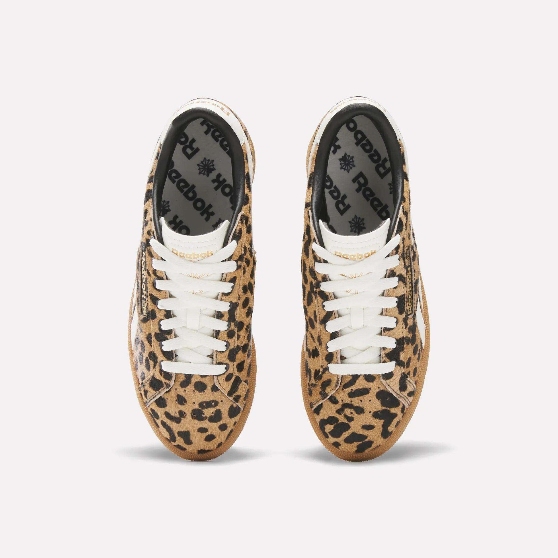 A pair of Reebok Women's Club C Grounds UK Shoes with a tan and black leopard print, white laces, and black Reebok insoles is seen from above on a plain white background.