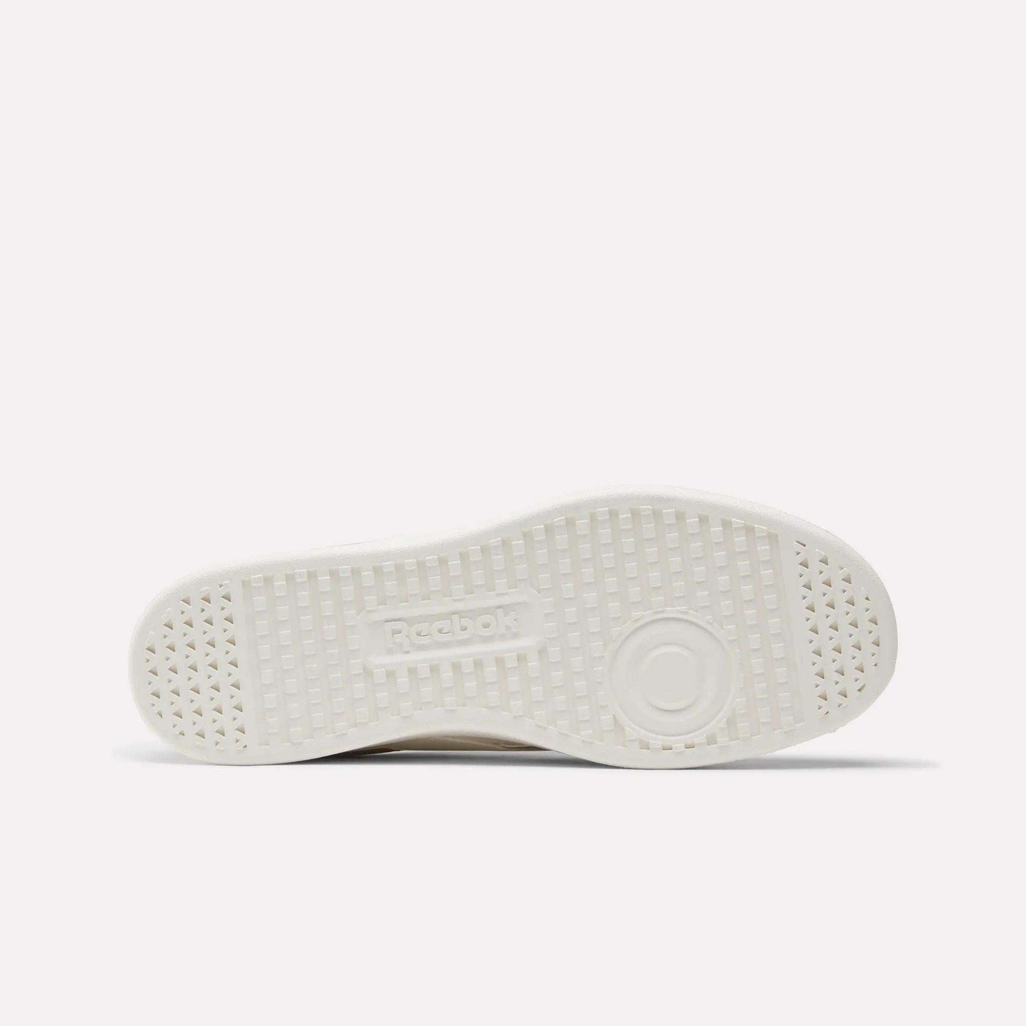 This image displays the white, textured rubber sole of Reebok's Smash Edge Shoes from below, highlighting small triangular patterns, circular tread details, and an embossed Reebok logo in the center.