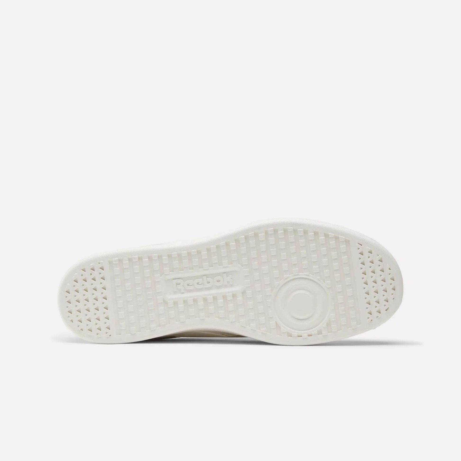 This image displays the white, textured rubber sole of Reebok's Smash Edge Shoes from below, highlighting small triangular patterns, circular tread details, and an embossed Reebok logo in the center.