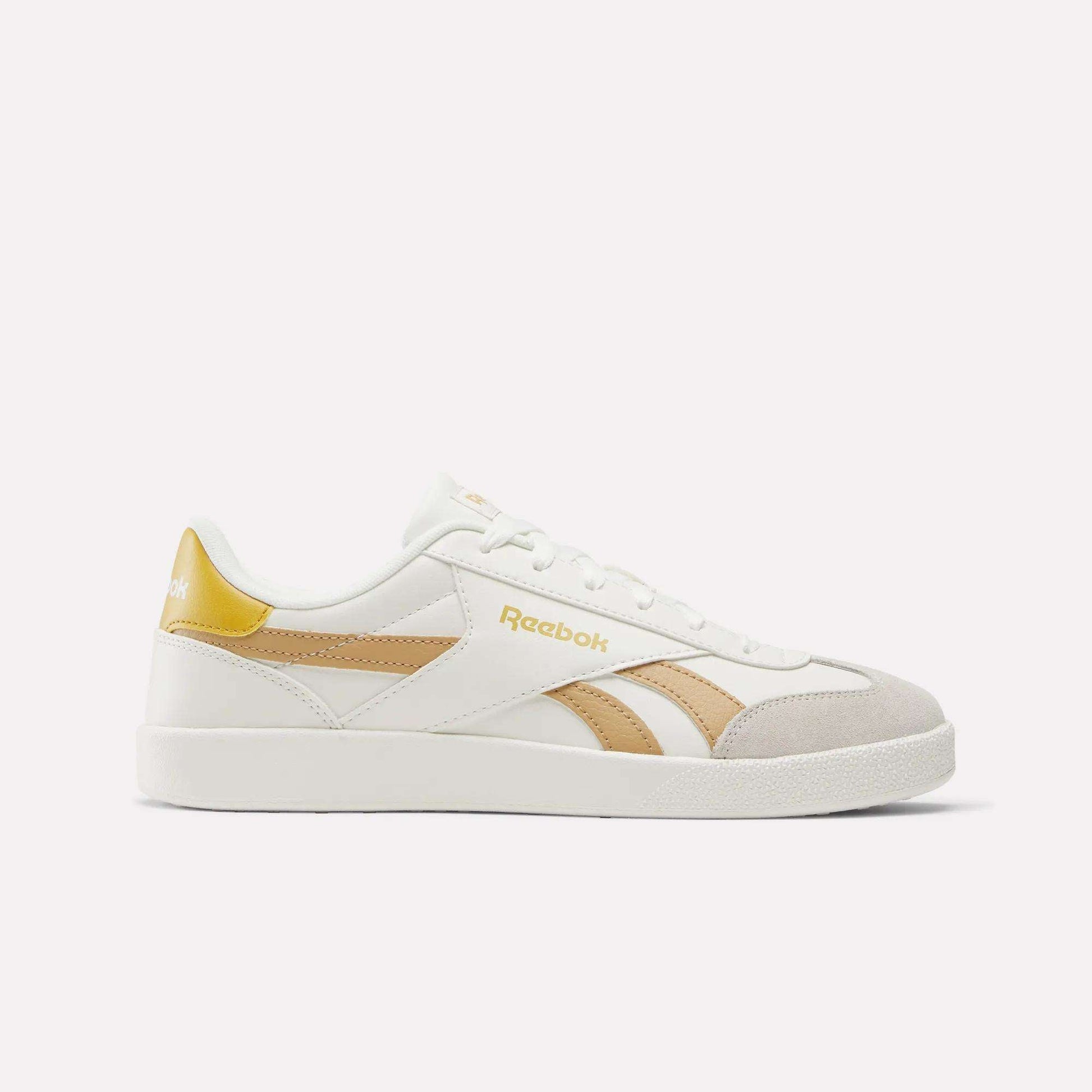 The Reebok Smash Edge Shoes feature a white design with beige and gold accents and the Reebok logo on the side and heel—ideal for fans of classic indoor soccer style, shown against a plain white background.