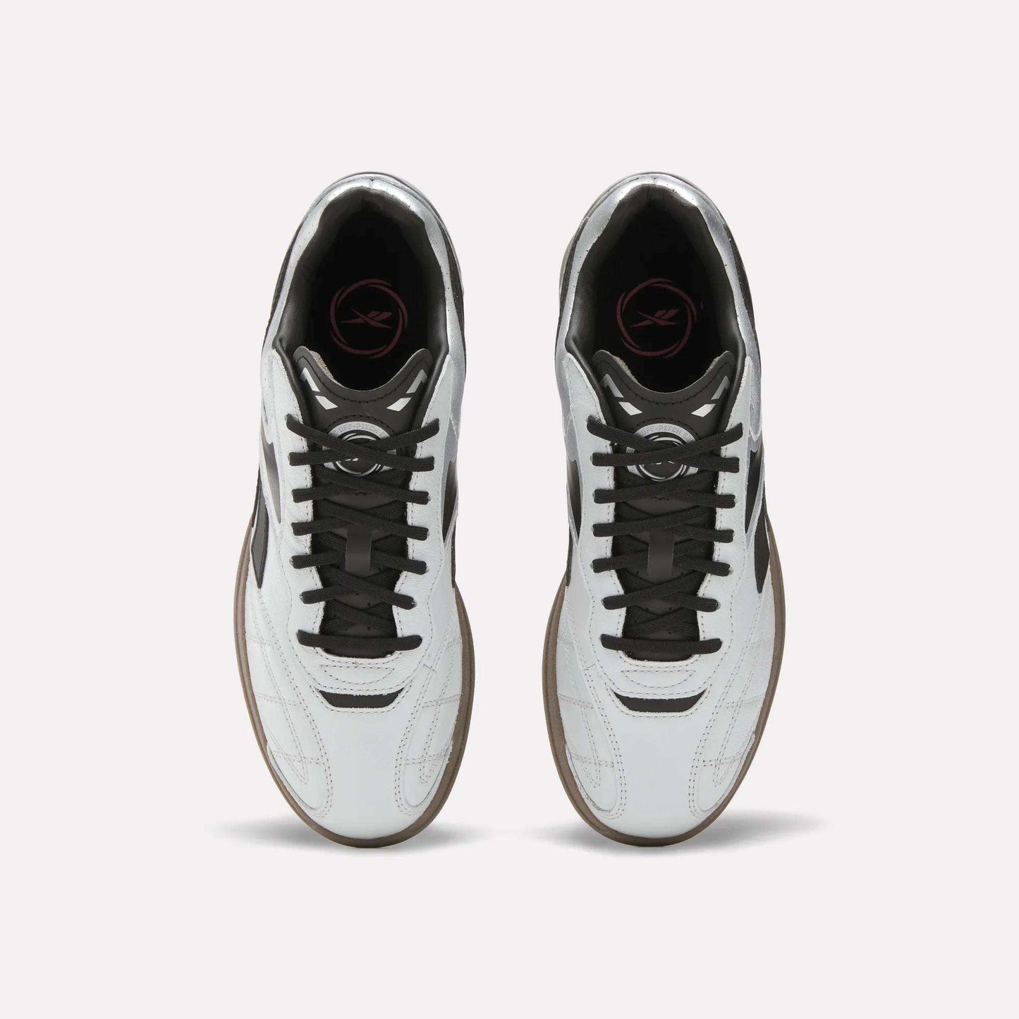 Top view of Reebok Hammer Street Shoes—soccer-inspired full-grain leather shoes with black laces, brown soles, and a pink logo on the black insole—placed side by side on a light background.