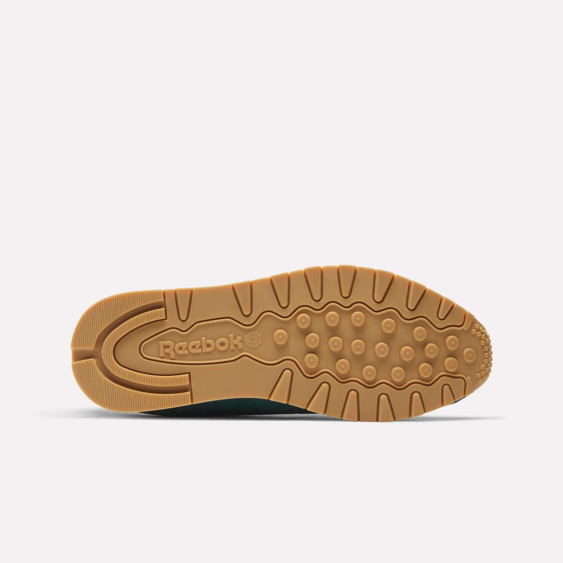 The image displays the light brown rubber sole of Reebok Classic Leather Shoes facing up, showing textured grip patterns and an embossed Reebok logo near the heel, all set against a plain white background.