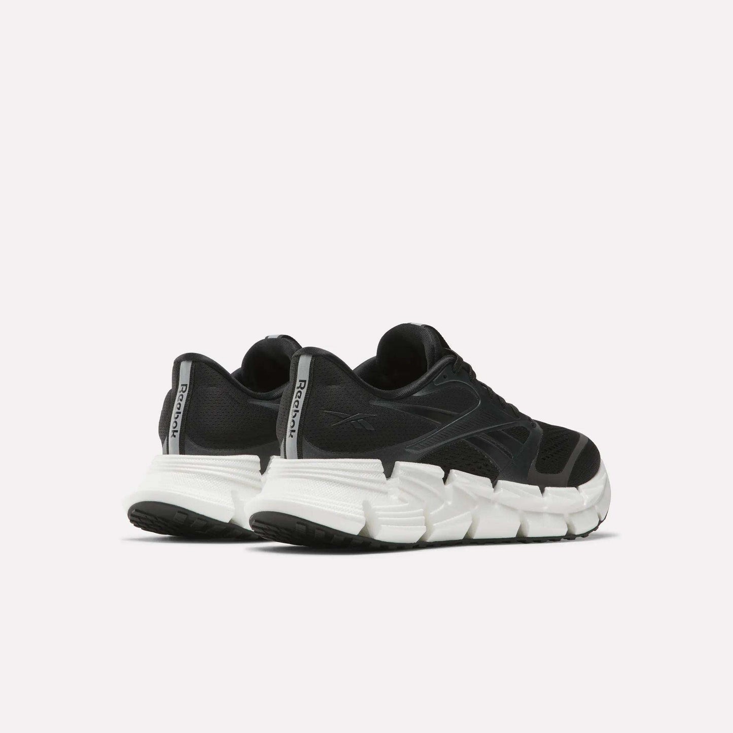 A pair of Reebok Women's FloatZig 2 Running Shoes in black with thick, white segmented soles and Superfloat+ cushioning, displayed from a rear side angle against a plain light background.