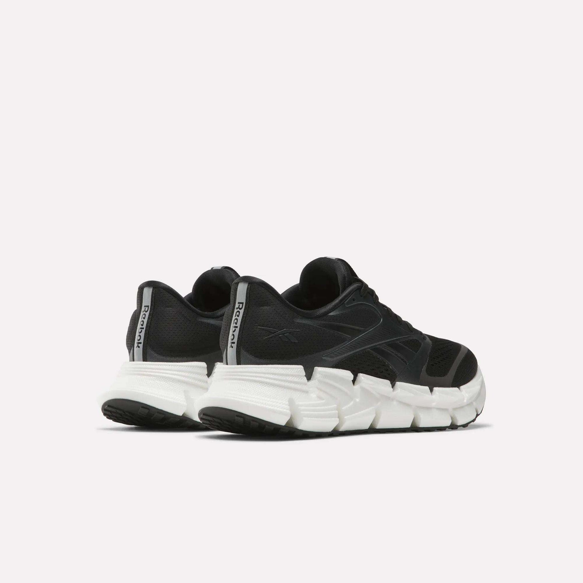 A pair of Reebok Women's FloatZig 2 Running Shoes in black with thick, white segmented soles and Superfloat+ cushioning, displayed from a rear side angle against a plain light background.