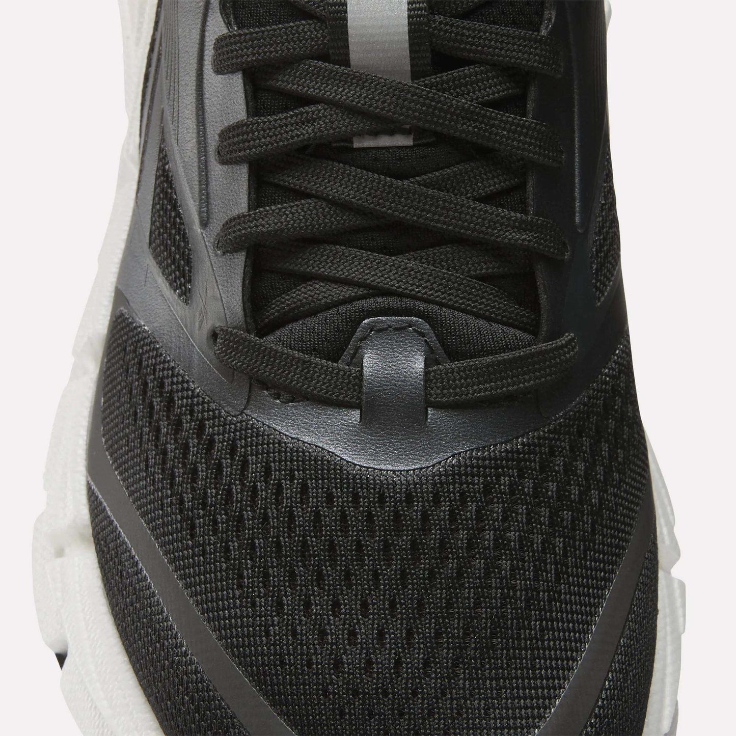 Close-up of the upper part of the Reebok Women's FloatZig 2 Running Shoe in black with mesh fabric, black laces, and gray and white accents on a white sole, featuring Superfloat+ cushioning for comfort.