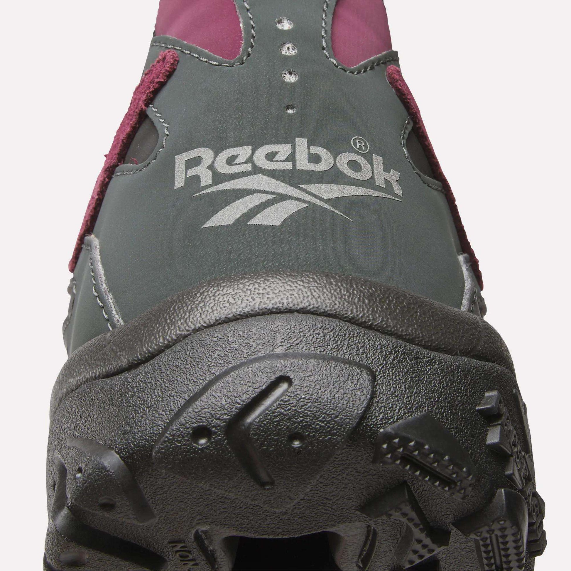 Close-up of the front of a dark grey Reebok Preseason 94 Low Retro Basketball Shoe, featuring a white Reebok logo on the upper, maroon accents, and a rugged black sole—a modern update to classic '90s style.
