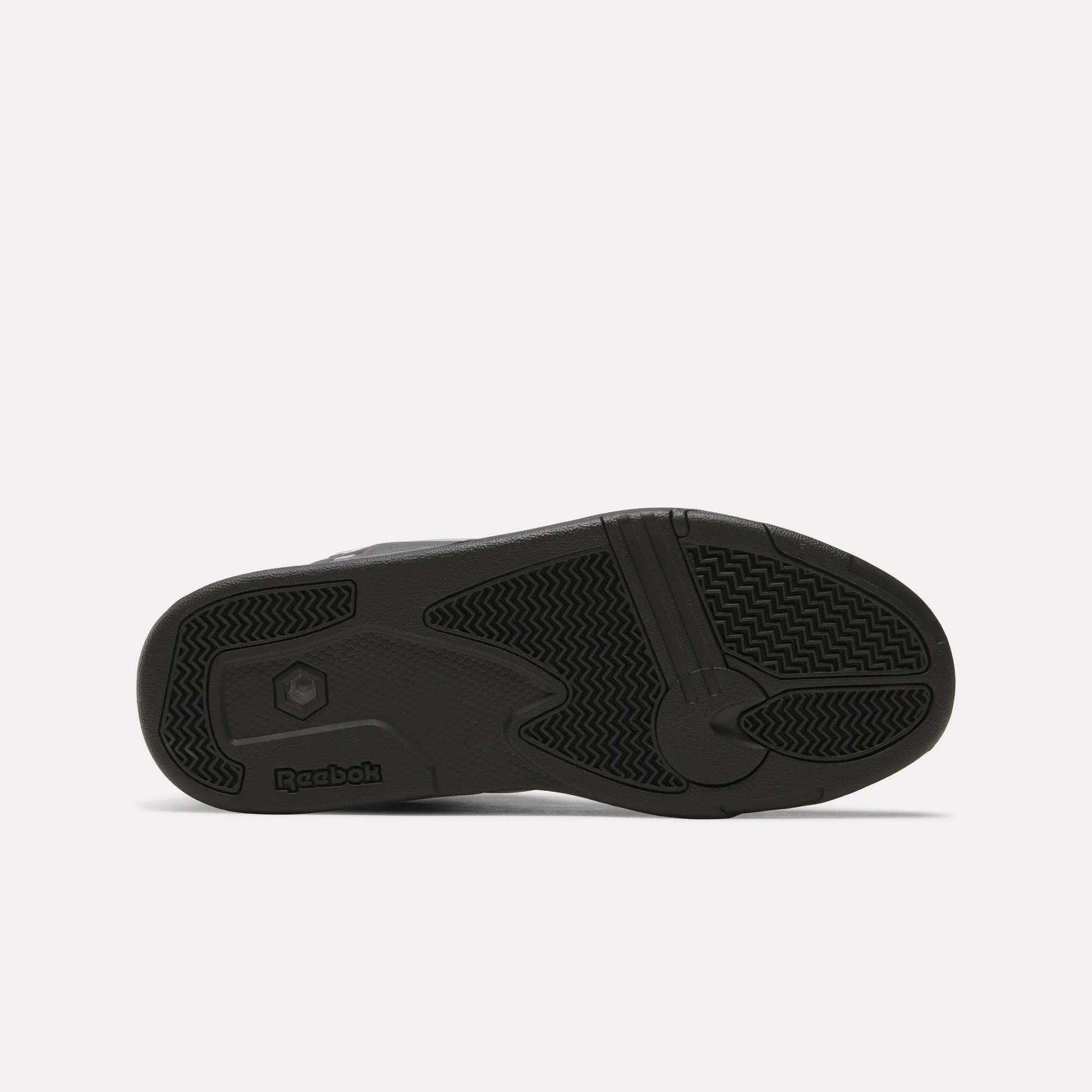 The image shows the black rubber outsole of the Reebok Pump Omni Zone II Retro Basketball Shoes, with textured grip patterns and a Reebok logo by the heel. The background is plain and light-colored.