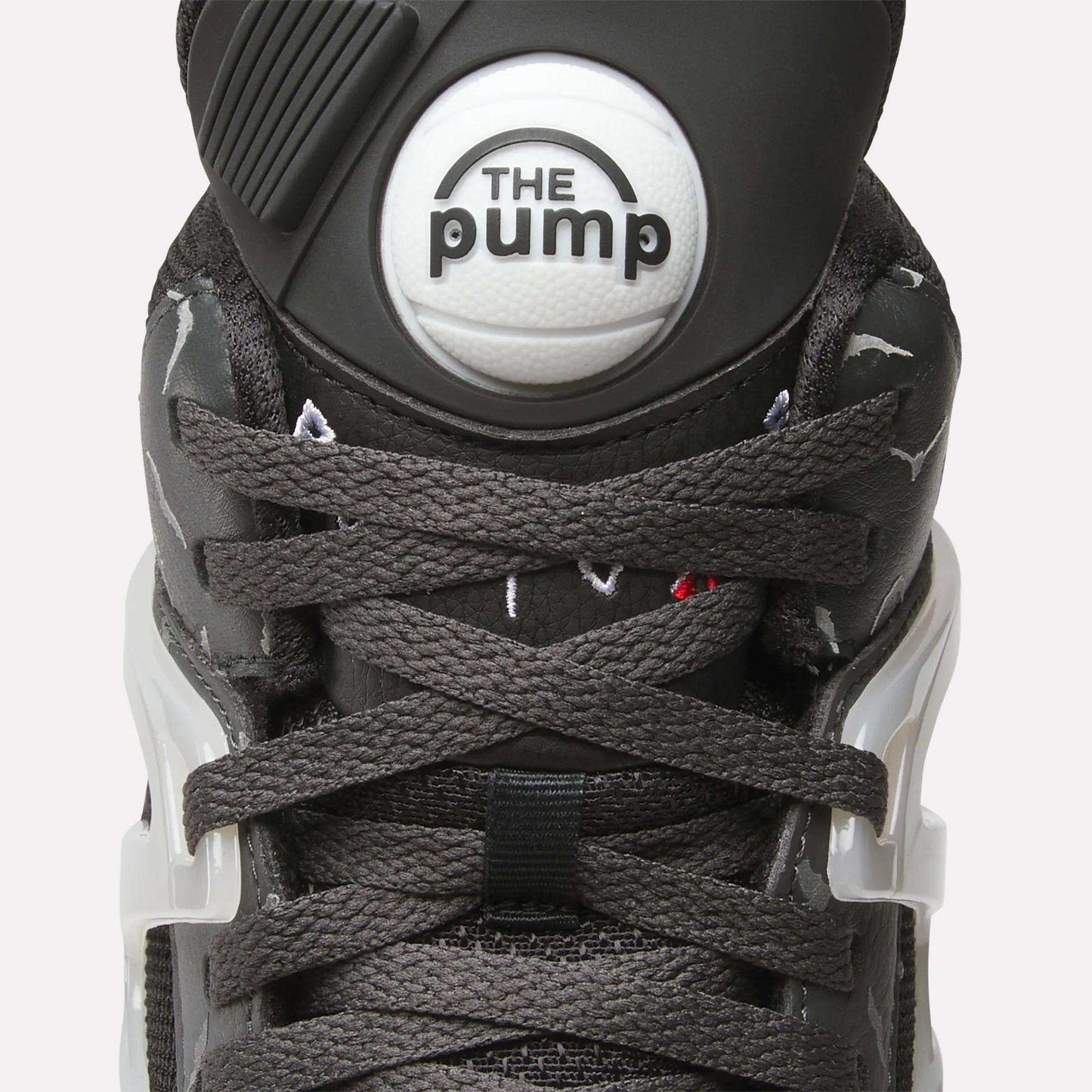 Close-up of Reebok Pump Omni Zone II Retro Basketball Shoes featuring dark gray laces, a round white "The Pump" button on the tongue, white plastic lace holders, and subtle reflective accents on the sides.