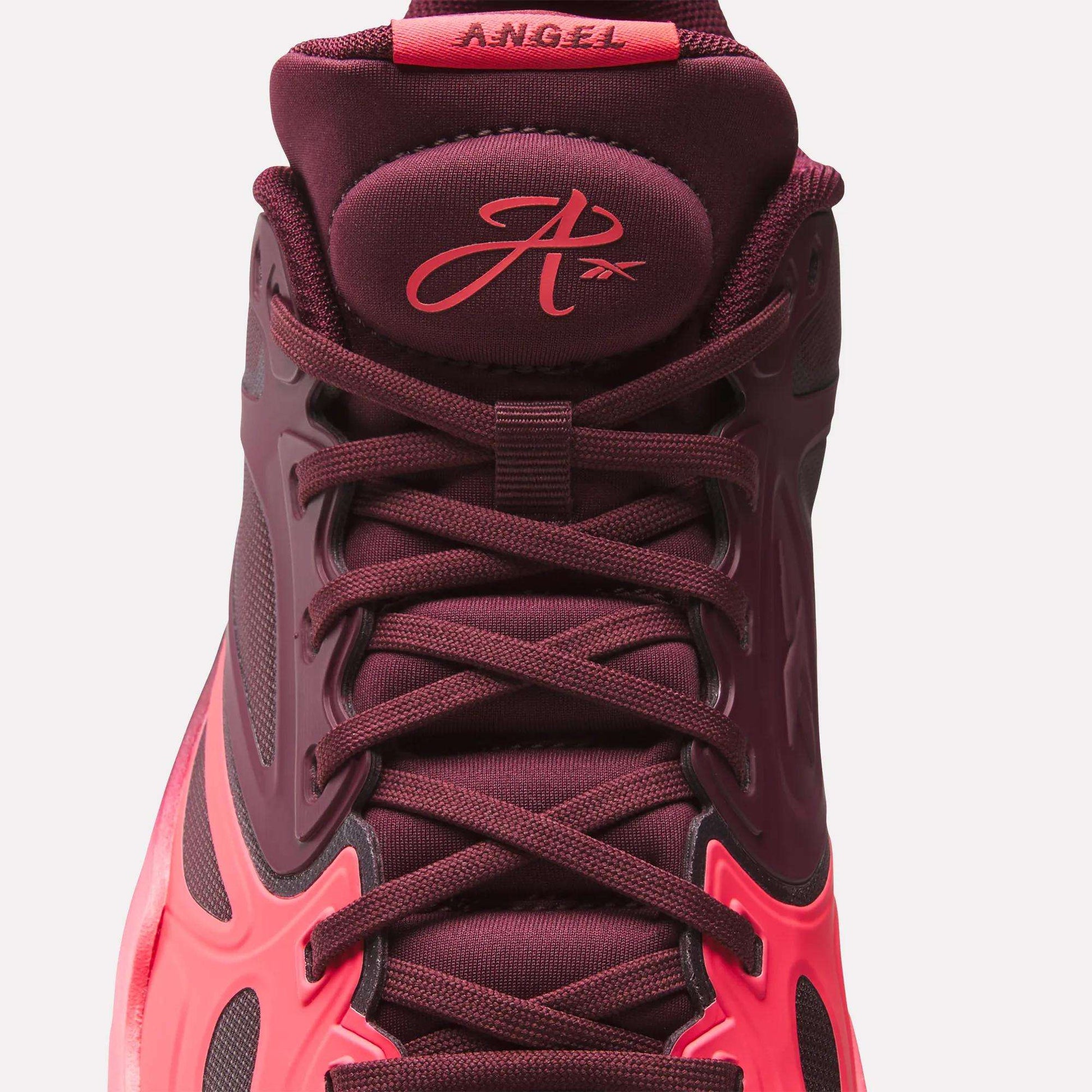A close-up of the Reebok Engine A Basketball Shoes in burgundy and pink, showcasing the laces, tongue with a stylized A logo and "ANGEL" label—featuring SuperFloat foam for extra comfort.