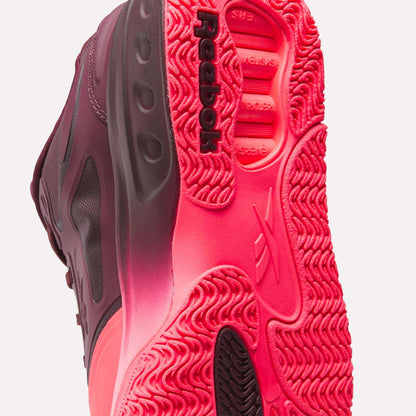 Close-up view of the sole of Reebok's Engine A Basketball Shoes, featuring bright pink and black textured rubber, SuperFloat foam for comfort, and the Reebok logo near the heel.
