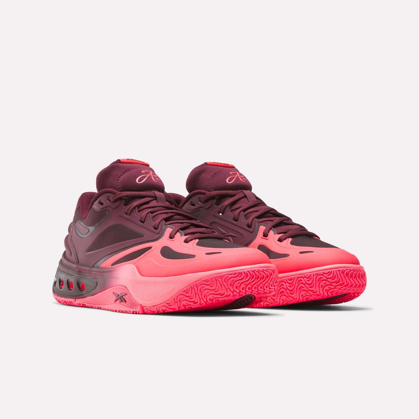 The Reebok Engine A Basketball Shoes are low-top athletic sneakers in red and pink, featuring SuperFloat foam for comfort, textured soles, a modern pattern, and branding on the tongues and sides.