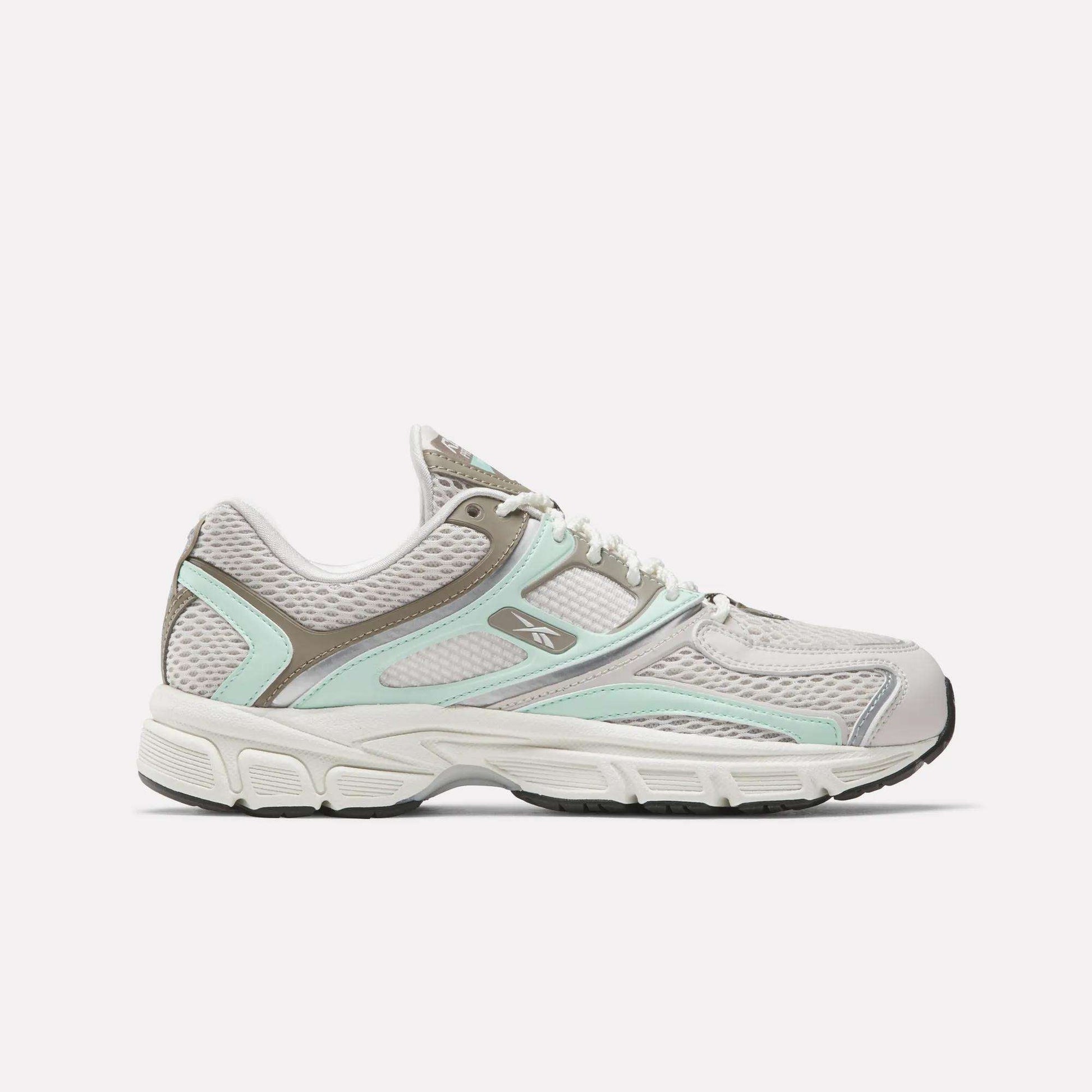 The Reebok Women's Premier Trinity Shoes are shown in a side profile, featuring gray and white colors with light aqua and taupe accents, mesh panels, and a black sole, blending retro tech style with modern design against a plain background.
