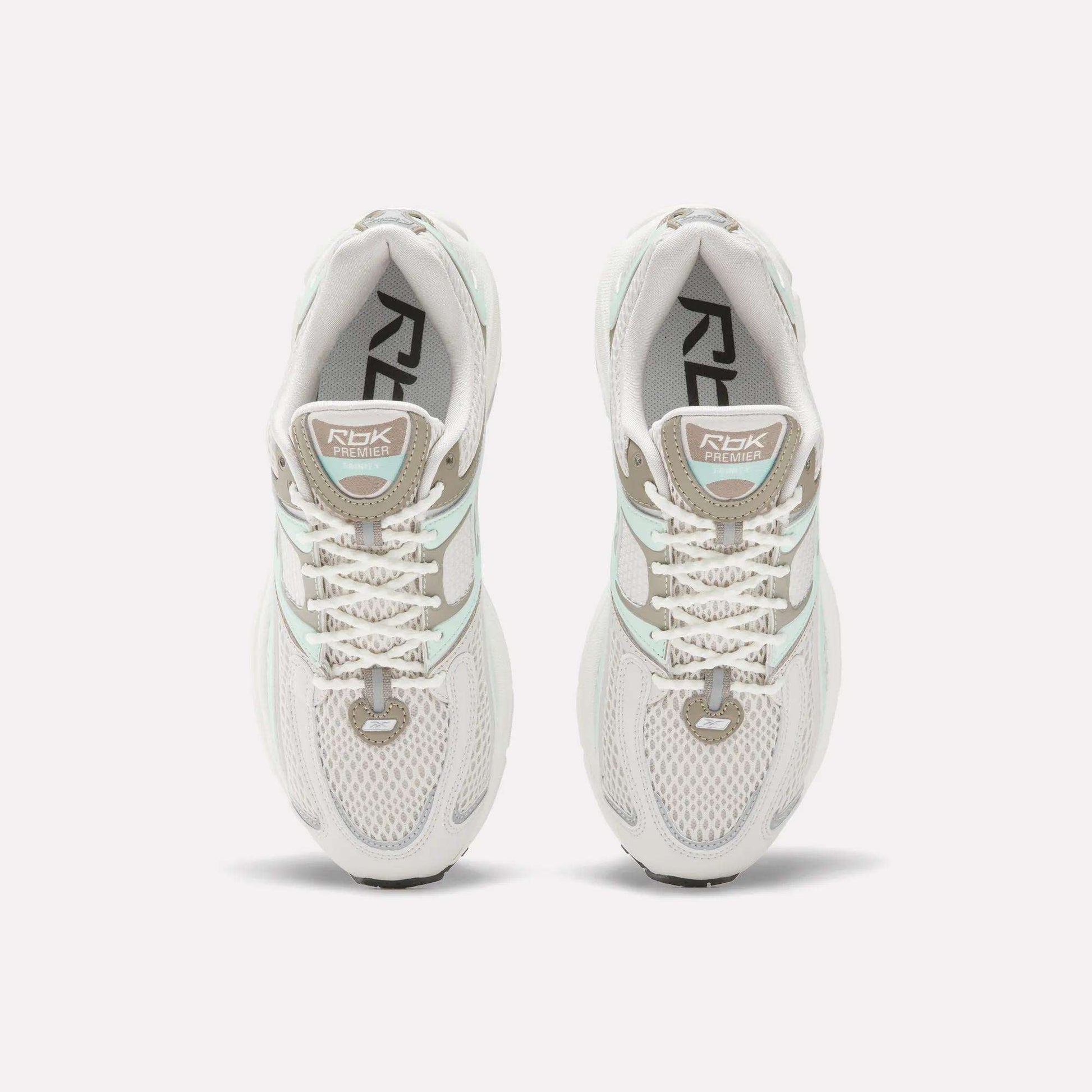 Top view of Reebok Women's Premier Trinity Shoes in white with gray and light green accents, mesh panels, and RBK branding—highlighting retro tech style on a clean white background.