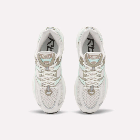 Top view of Reebok Women's Premier Trinity Shoes in white with gray and light green accents, mesh panels, and RBK branding—highlighting retro tech style on a clean white background.