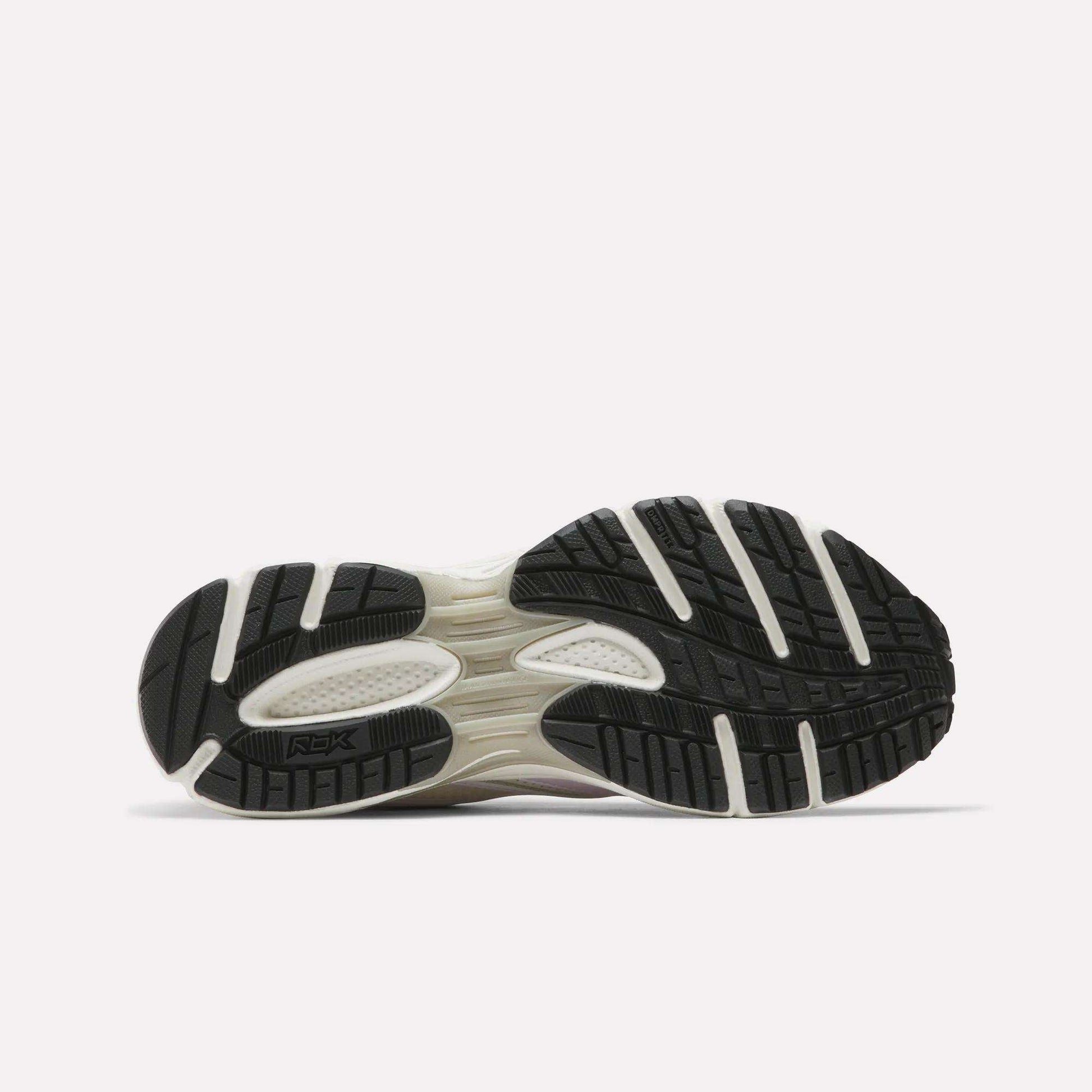 The image displays the black sole with white accents and textured tread of Reebok Women's Premier Trinity Shoes, highlighting their grip-focused design against a plain light background.