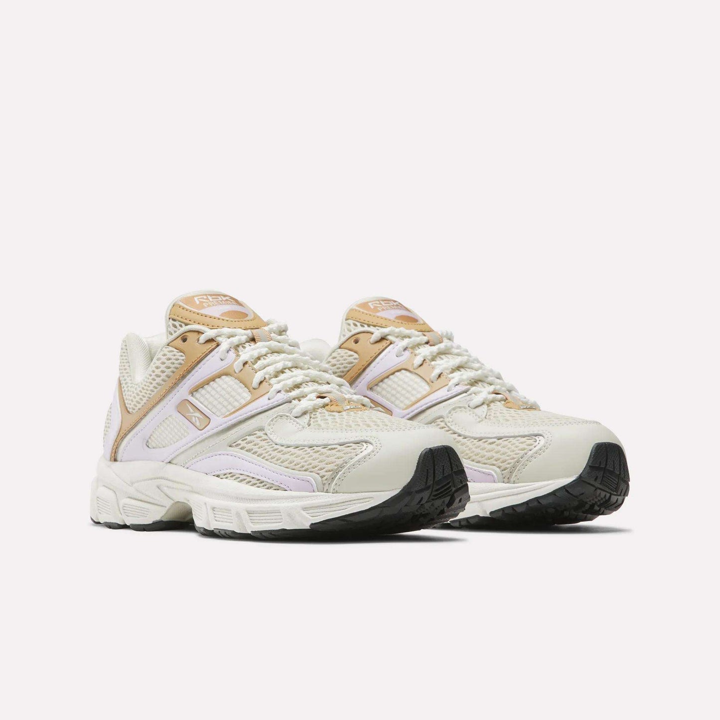 The Reebok Women's Premier Trinity Shoes feature beige and white uppers with tan accents, mesh panels, and chunky black soles, blending retro tech style with modern comfort. Displayed on a plain white background.