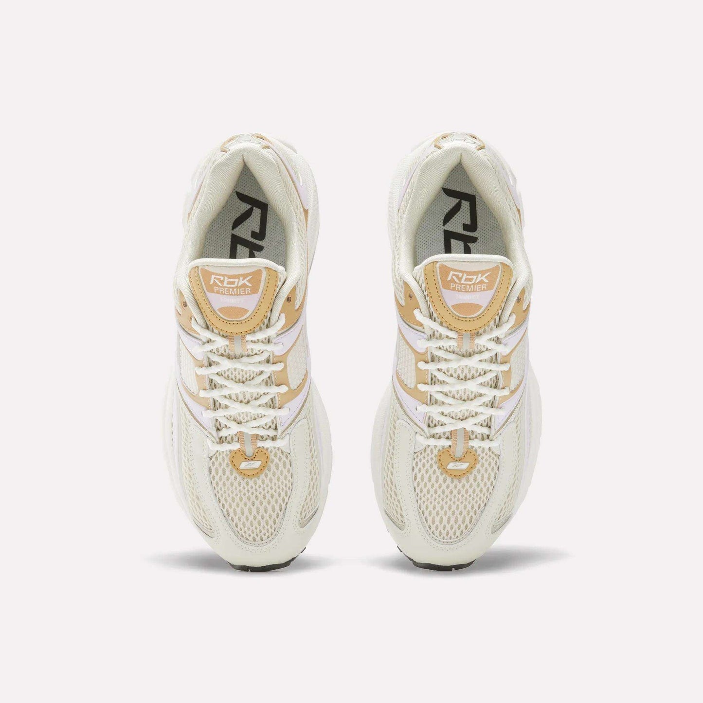 Top view of Women's Premier Trinity Shoes by Reebok in cream and beige, featuring white laces, mesh uppers, and branded tongues, inspired by retro tech running shoes, displayed on a white background.
