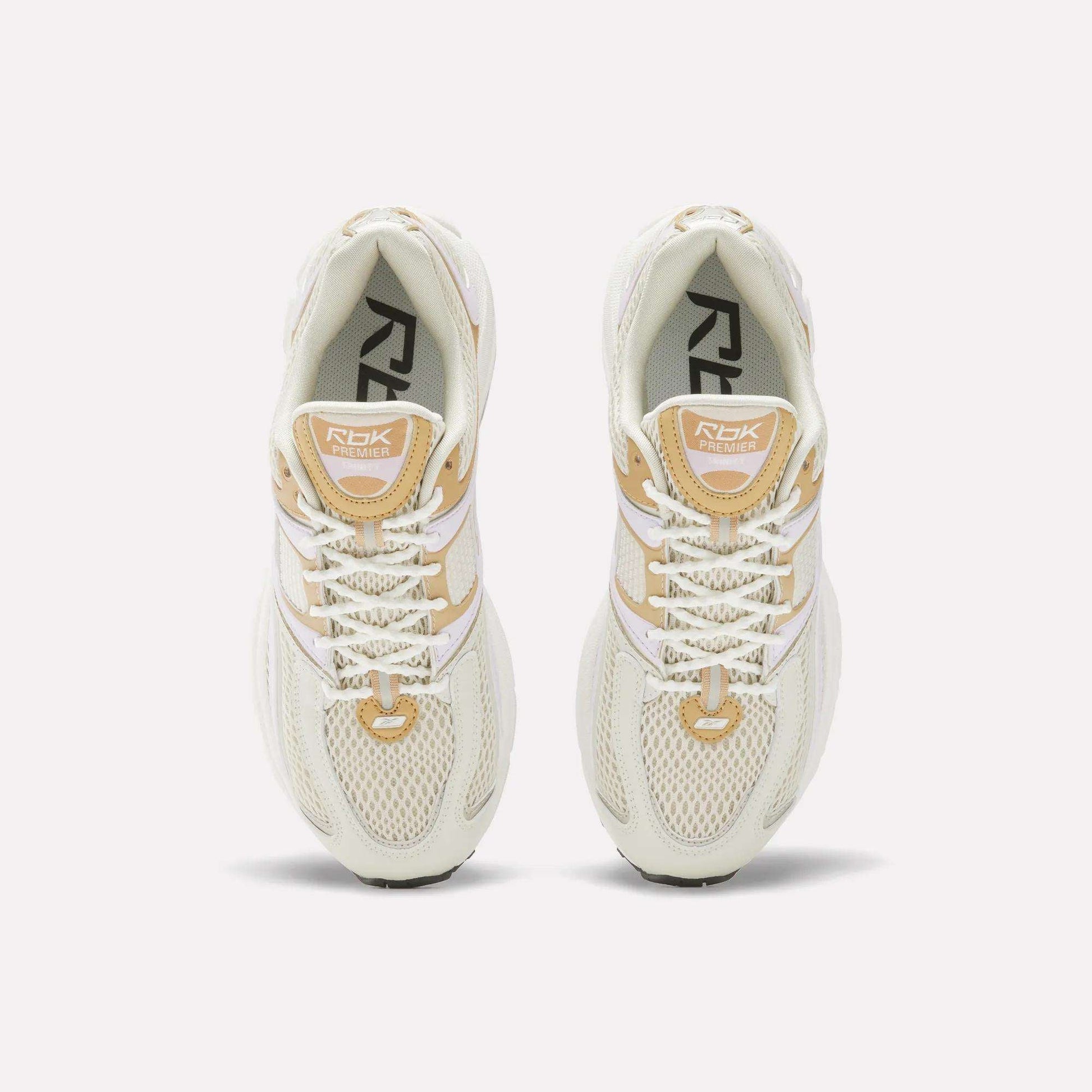 Top view of Women's Premier Trinity Shoes by Reebok in cream and beige, featuring white laces, mesh uppers, and branded tongues, inspired by retro tech running shoes, displayed on a white background.