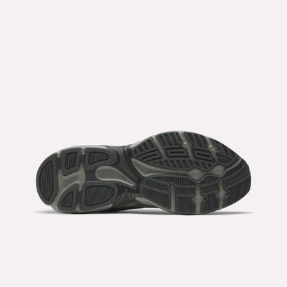 The image shows the sole of Reebok Premier Road Control Shoes, mainly black and gray, with textured rubber patterns and grooves for traction. The Reebok logo appears near the center, reflecting these classic retro running shoes.
