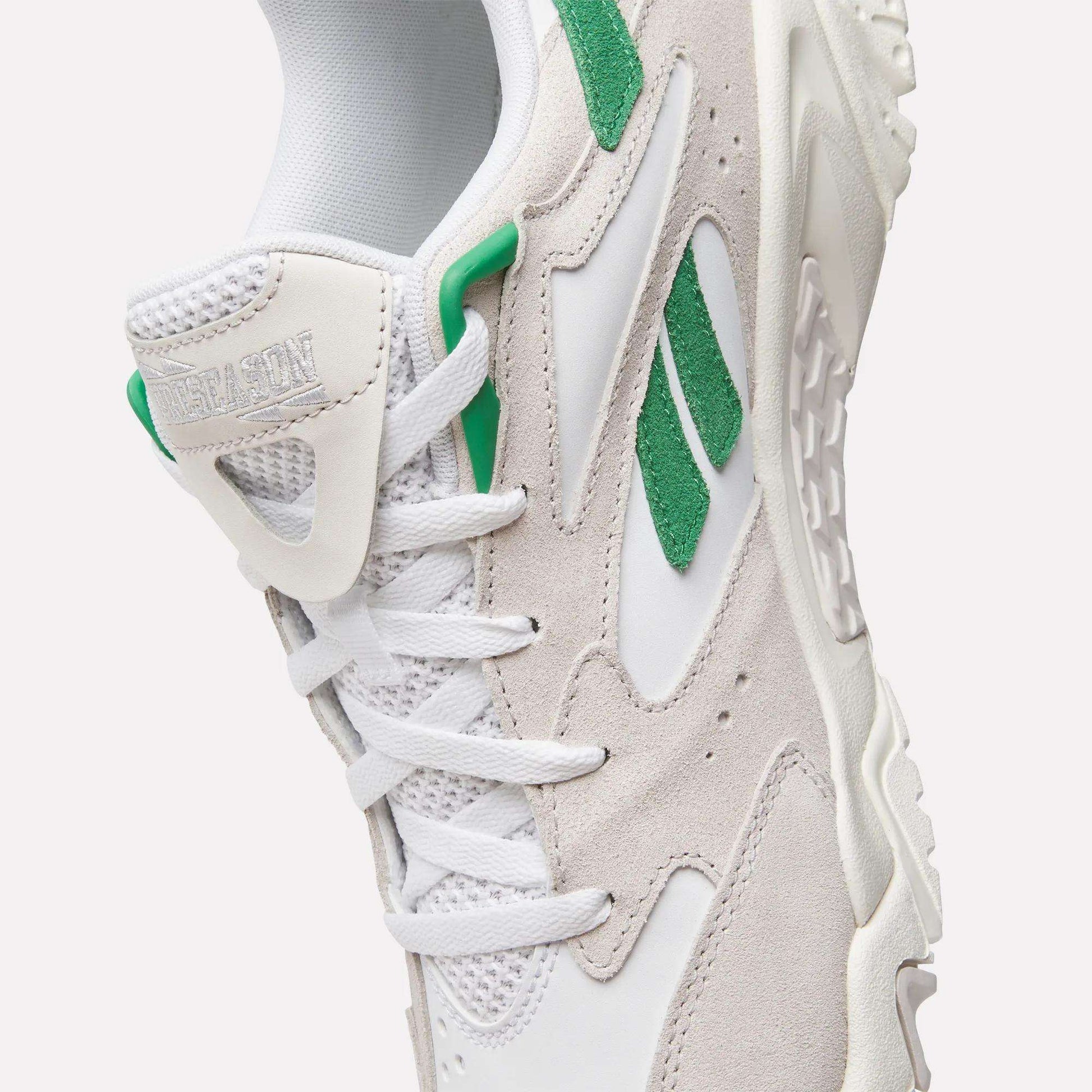A close-up of the Reebok Preseason 94 Low Retro Basketball Shoes, featuring white and light gray tones, green suede accents, white laces, textured sole, and visible Reebok logos—blending '90s archive style with modern training performance.