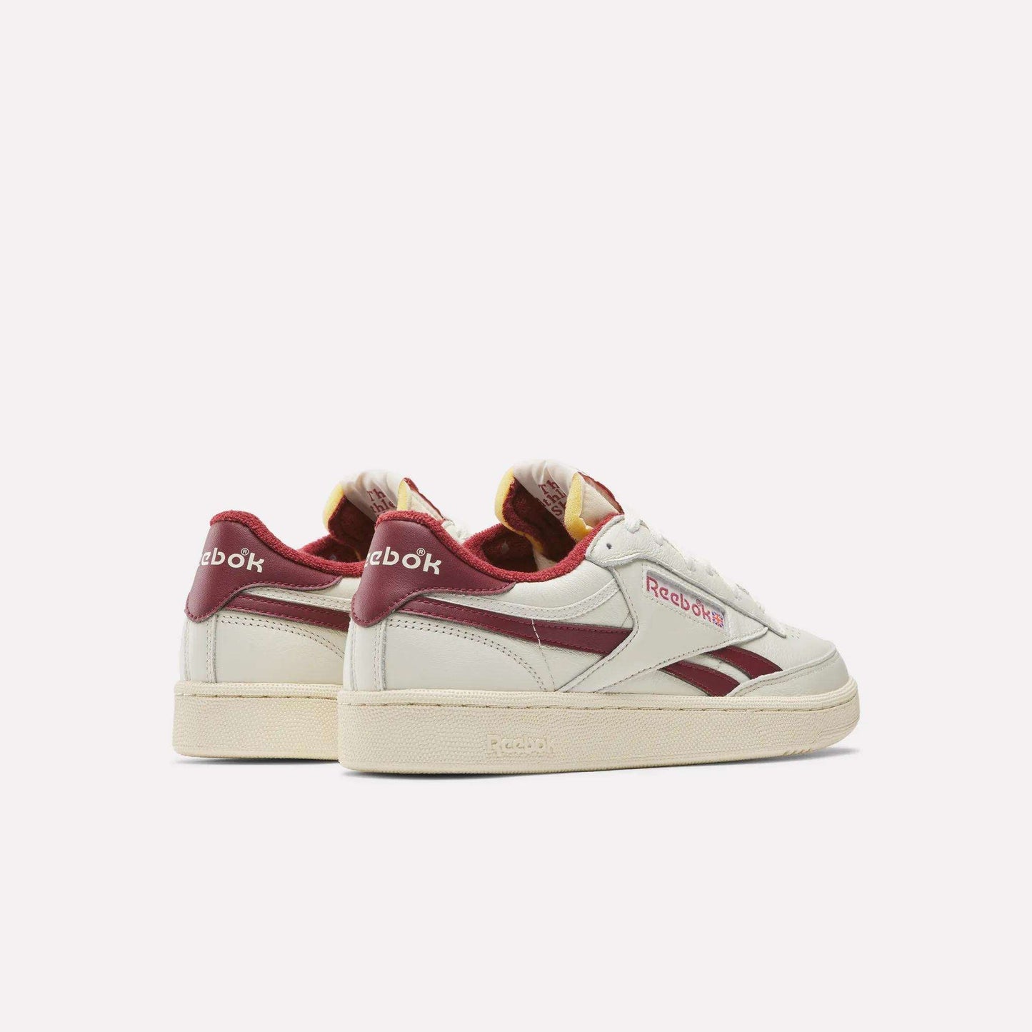 The Reebok Club C Revenge Vintage Shoes, made from full-grain leather, are shown from the back and side in white with burgundy accents and logo, displayed against a plain light background.