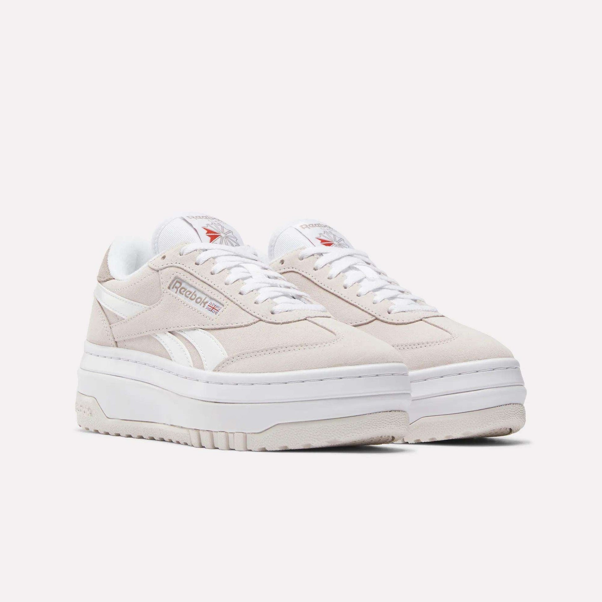 A pair of Women's Campio Extra Shoes by Reebok in beige, featuring white accents, thick white soles, white laces, and the Reebok logo on the sides and tongue, displayed on a plain white background.