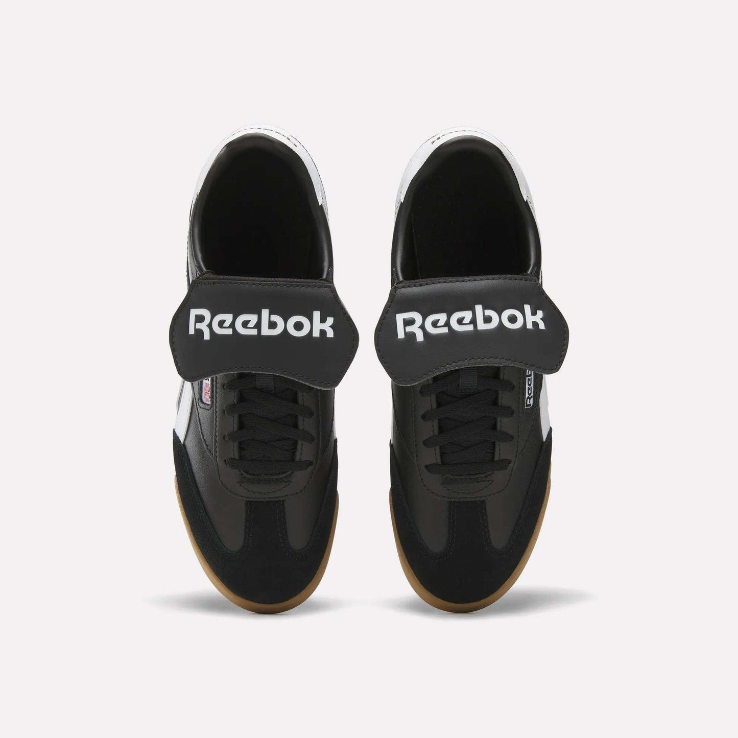 Top view of Reebok Campio XT Kilty Shoes in black with wide Velcro straps, white Reebok logo, black laces, and light brown soles. These tennis-inspired sneakers are shown on a plain white background.