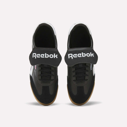 Top view of Reebok Campio XT Kilty Shoes in black with wide Velcro straps, white Reebok logo, black laces, and light brown soles. These tennis-inspired sneakers are shown on a plain white background.