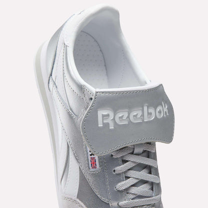 Close-up of Reebok Campio XT Kilty Shoes in gray and white with white laces, embossed Reebok logo on the tongue, and a small Union Jack label on the side, highlighting their classic tennis-inspired style.