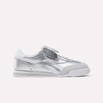 A pair of Reebok Campio XT Kilty Shoes featuring silver color, white and gray accents, tennis-inspired low-top design, and the Reebok logo on the side, showcased against a plain white background.
