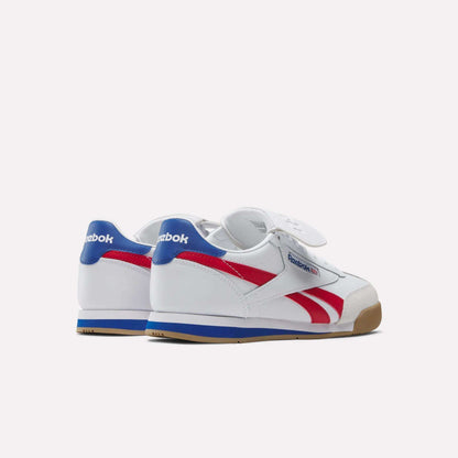 The Reebok Campio XT Kilty Shoes, made of white leather with blue heel tabs, red side stripes, and gum soles, are angled on a plain white background to highlight their tennis-inspired style.