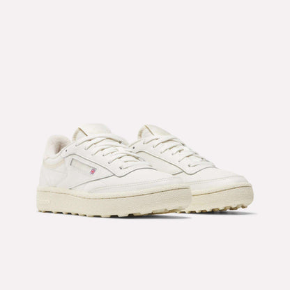 The Reebok Women's Club C Golf Shoes feature off-white water-resistant leather, textured rubber soles, white laces, subtle stitching, a spikeless design, and a small red and blue logo on the side.