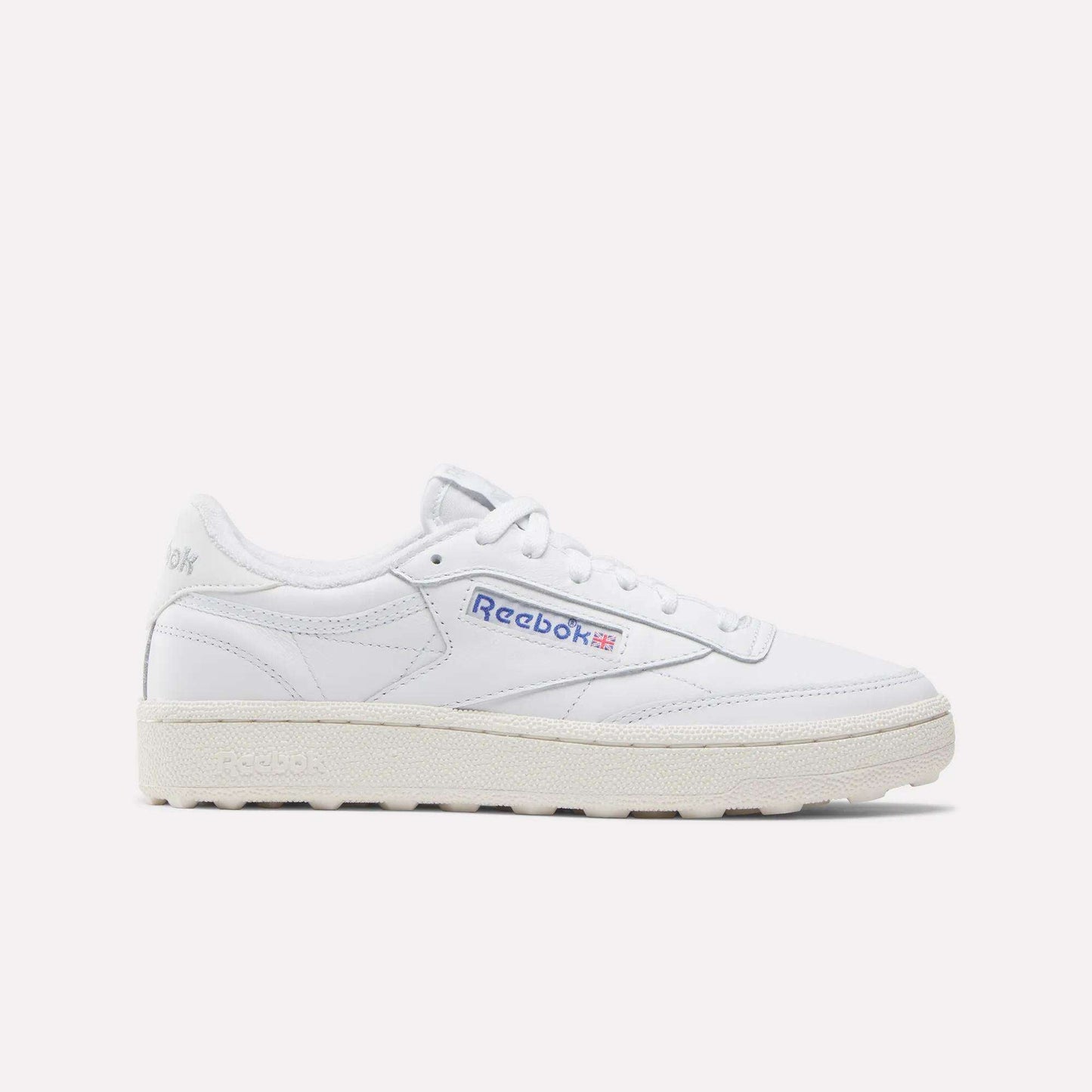 The Reebok Women’s Club C Golf Shoes feature a white upper, cream sole, blue and red side logo, spikeless outsole, and white laces, shown against a plain white background.