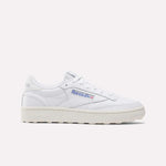 The Reebok Women’s Club C Golf Shoes feature a white upper, cream sole, blue and red side logo, spikeless outsole, and white laces, shown against a plain white background.