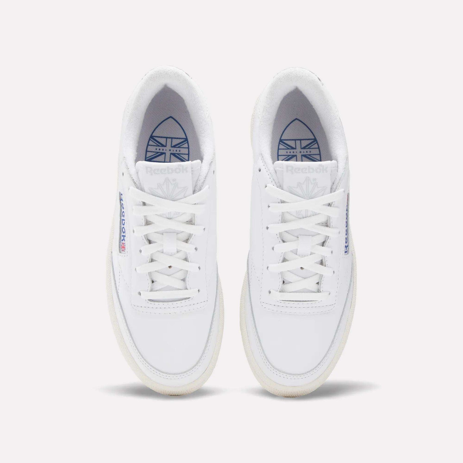 Top view of Reebok Women's Club C Golf Shoes in water-resistant leather, featuring white sneakers with blue and red branding on the tongue and side, displayed side by side on a plain white background.