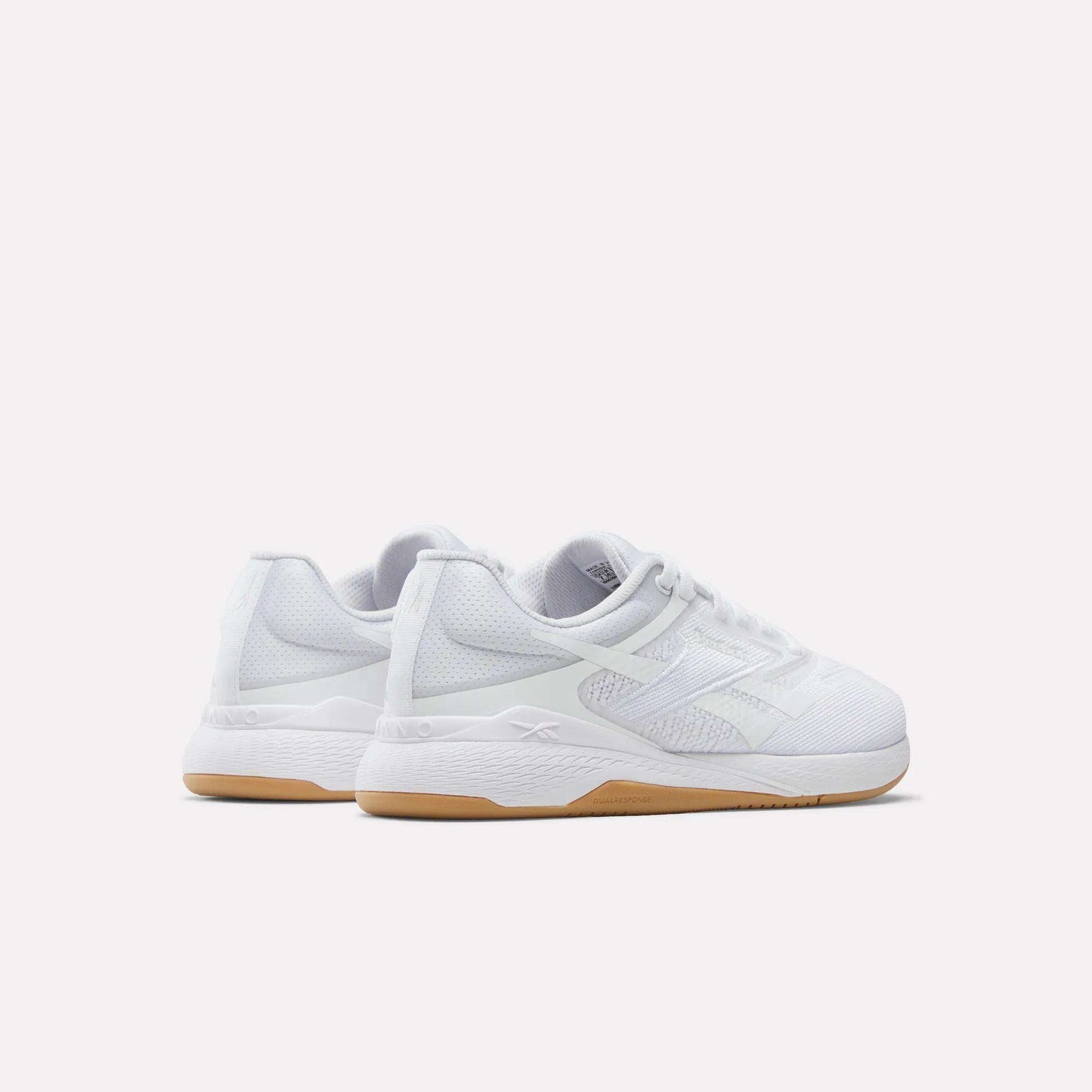 The Reebok Women's Nano X5 Training Shoes are white athletic sneakers with mesh uppers, white laces, and light brown rubber soles. Displayed against a plain background, both the heel and side views highlight their comfortable design.