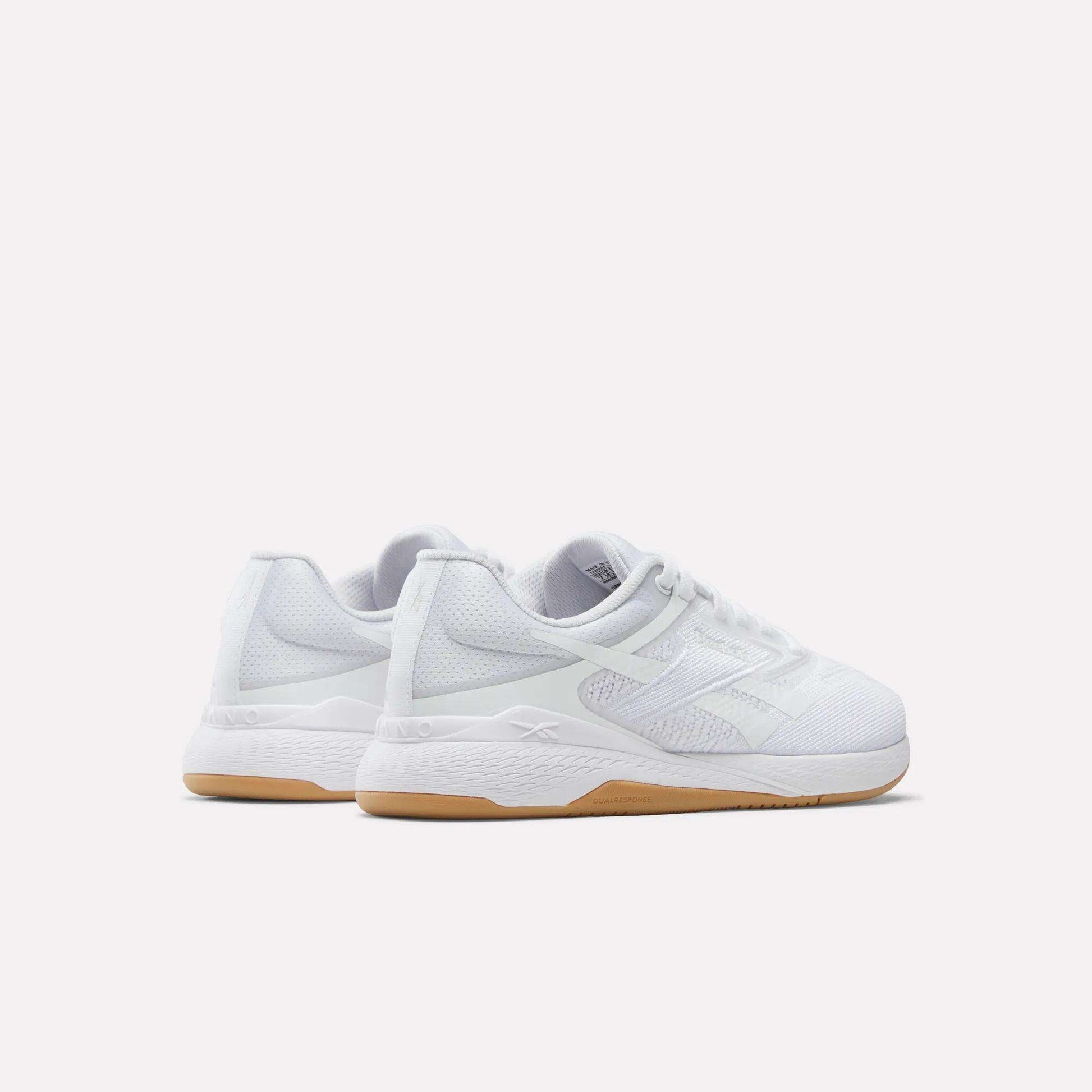 The Reebok Women's Nano X5 Training Shoes are white athletic sneakers with mesh uppers, white laces, and light brown rubber soles. Displayed against a plain background, both the heel and side views highlight their comfortable design.