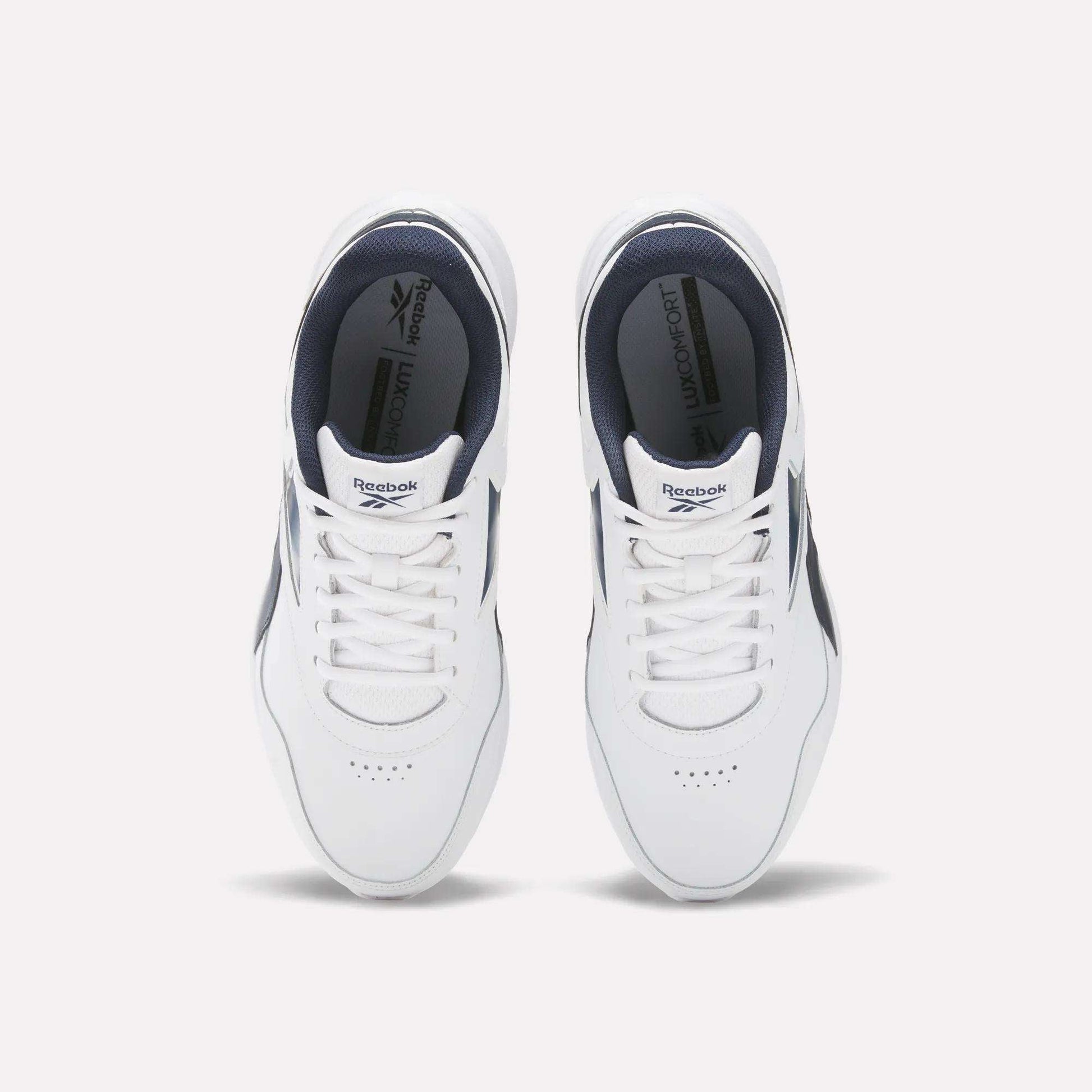 Top view of Reebok Men's Walk Ultra 7 DMX Max Wide 4E Shoes in white with navy accents and white laces, side by side on a light background. These wide-fit walking shoes offer comfort and style, featuring insoles with the Reebok logo.