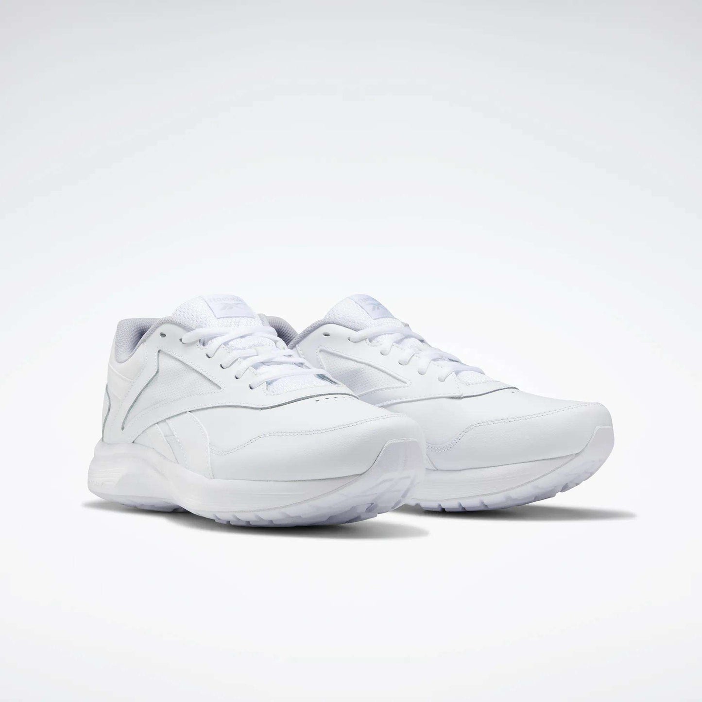 The Reebok Women's Walk Ultra 7 DMX Max Walking Shoes are shown in white on a light background, featuring a sleek minimalist design, white laces, DMX cushioned textured sole, and subtle stitched detailing.