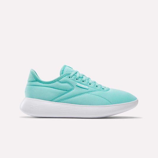 The Reebok Women's Active Lite Shoes feature a light teal upper, white sole, low-top silhouette, and DMX technology for comfort. The minimalist sneaker displays the Reebok logo near the laces and is shown in a side view against a white background.