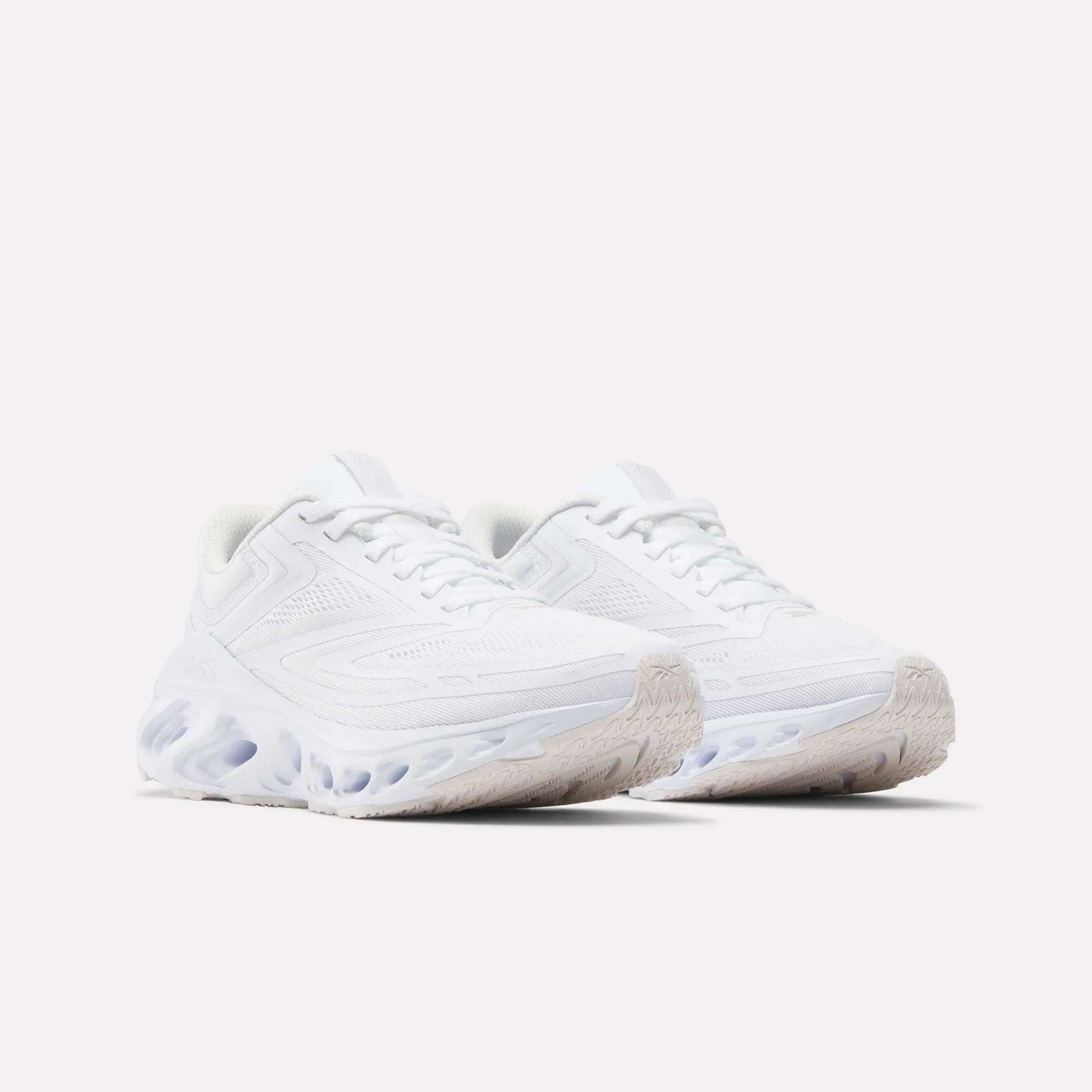 The Reebok Women's Fuel Flex Run Shoes in white feature textured soles and wavy Fuel Flex midsoles, shown against a light background.