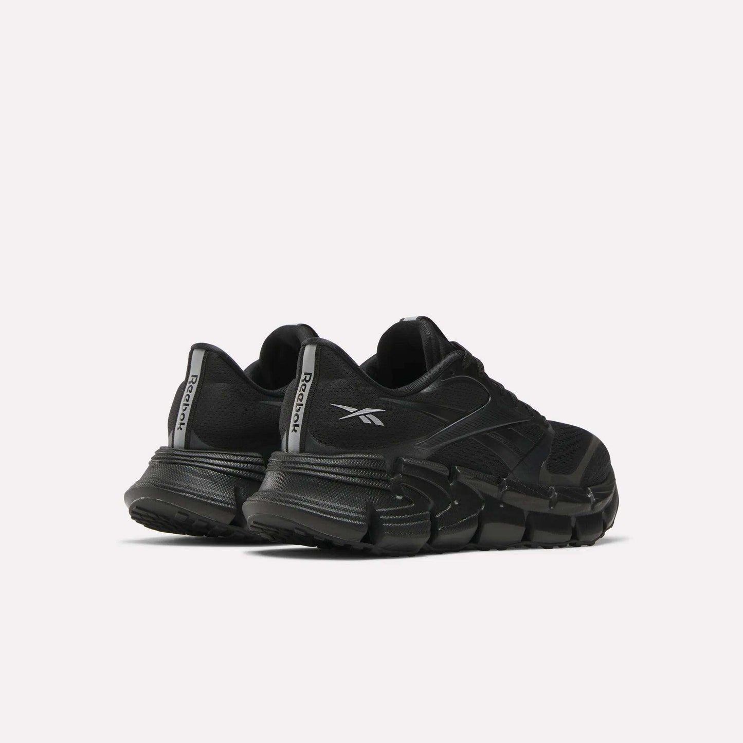 A pair of Women's FloatZig 2 Running Shoes by Reebok in black, with chunky soles and Superfloat+ cushioning, are shown from the back left side. The Reebok logo appears on the heel tabs against a plain light background.