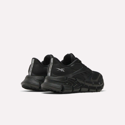 A pair of Women's FloatZig 2 Running Shoes by Reebok in black, with chunky soles and Superfloat+ cushioning, are shown from the back left side. The Reebok logo appears on the heel tabs against a plain light background.