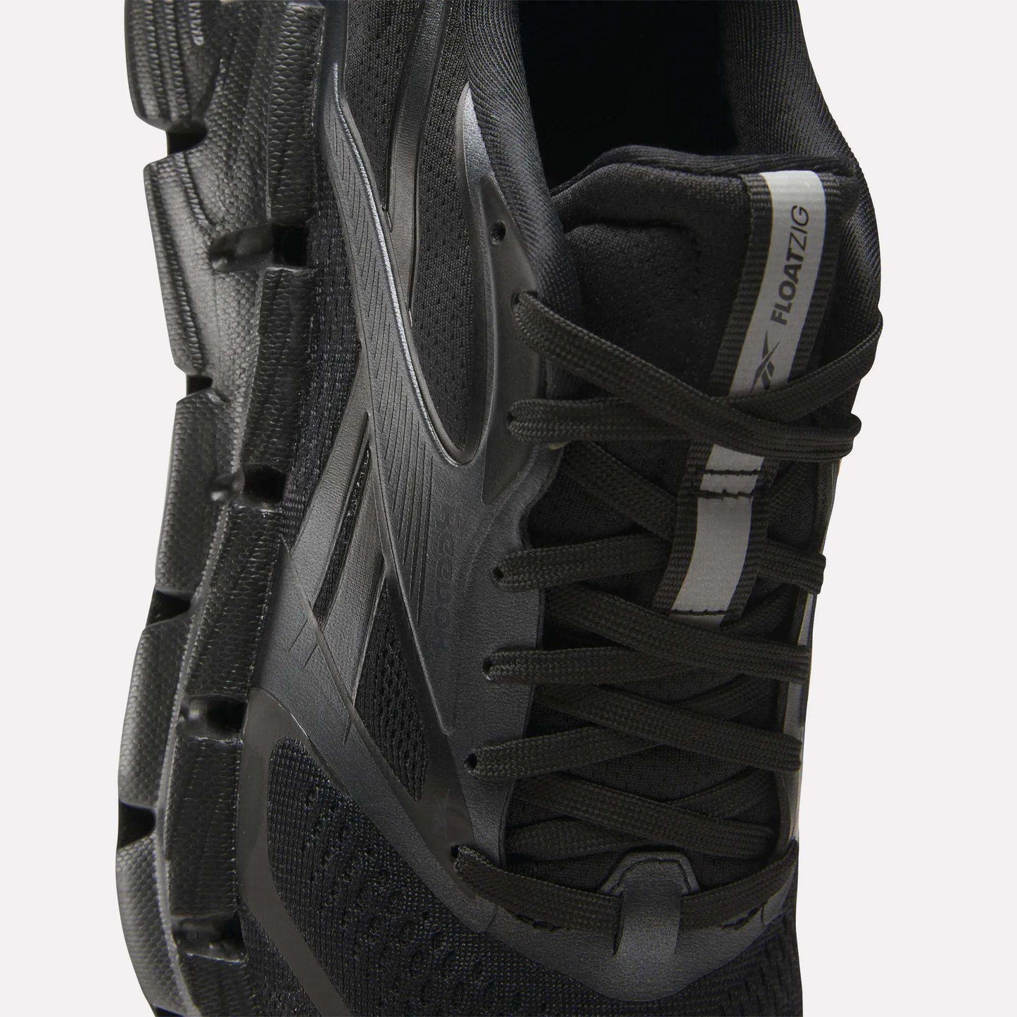 Close-up of a black Reebok Women's FloatZig 2 Running Shoe with energy-returning cushioning, mesh upper, black laces, zigzag-patterned sole, and a white and black tongue label reading ZIG KINETICA II FLOATZIG.