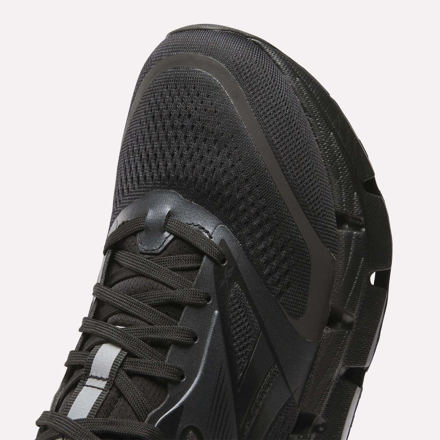 Close-up of the front and side of Reebok Men's FloatZig 2 Running Shoes in black, showing mesh fabric, laces, textured rubber sole, and energy-returning cushioning for enhanced comfort.