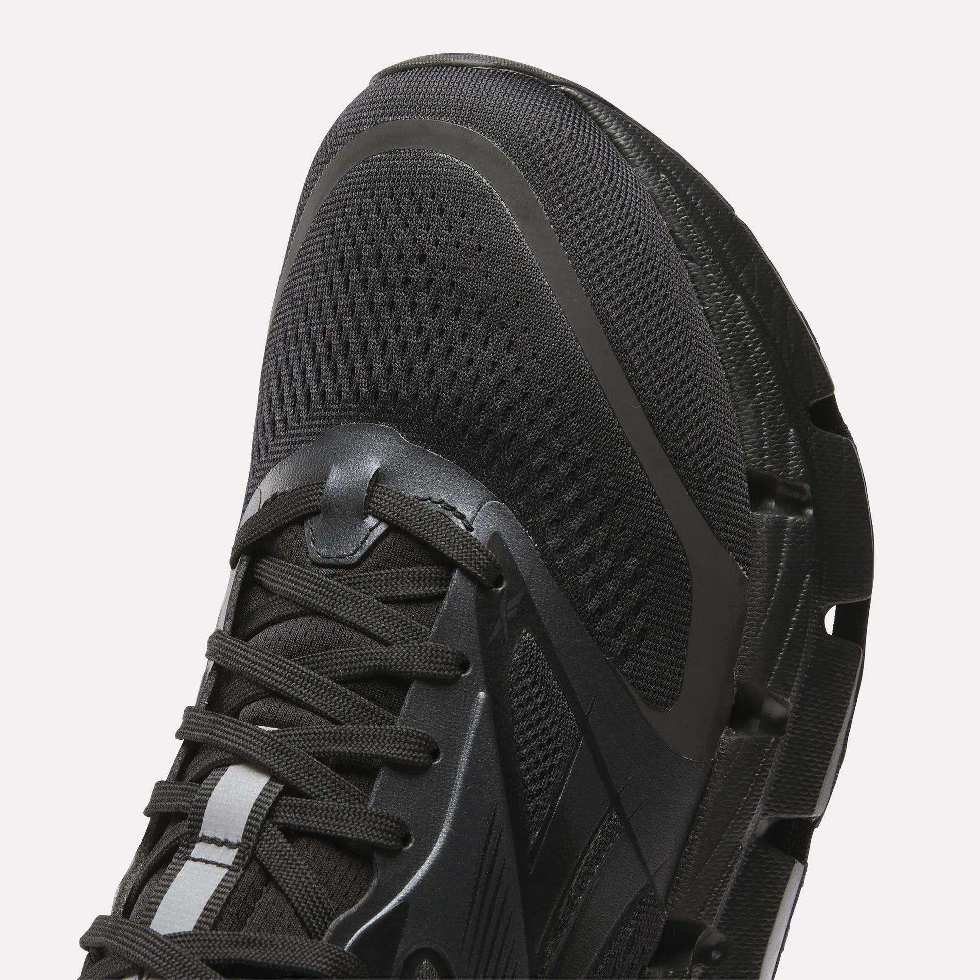 Close-up of the front and side of Reebok Men's FloatZig 2 Running Shoes in black, showing mesh fabric, laces, textured rubber sole, and energy-returning cushioning for enhanced comfort.