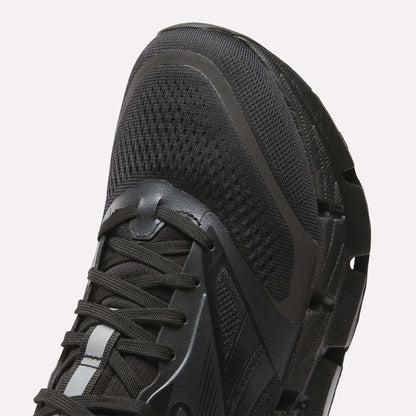 Close-up of the front and side of Reebok Men's FloatZig 2 Running Shoes in black, showing mesh fabric, laces, textured rubber sole, and energy-returning cushioning for enhanced comfort.