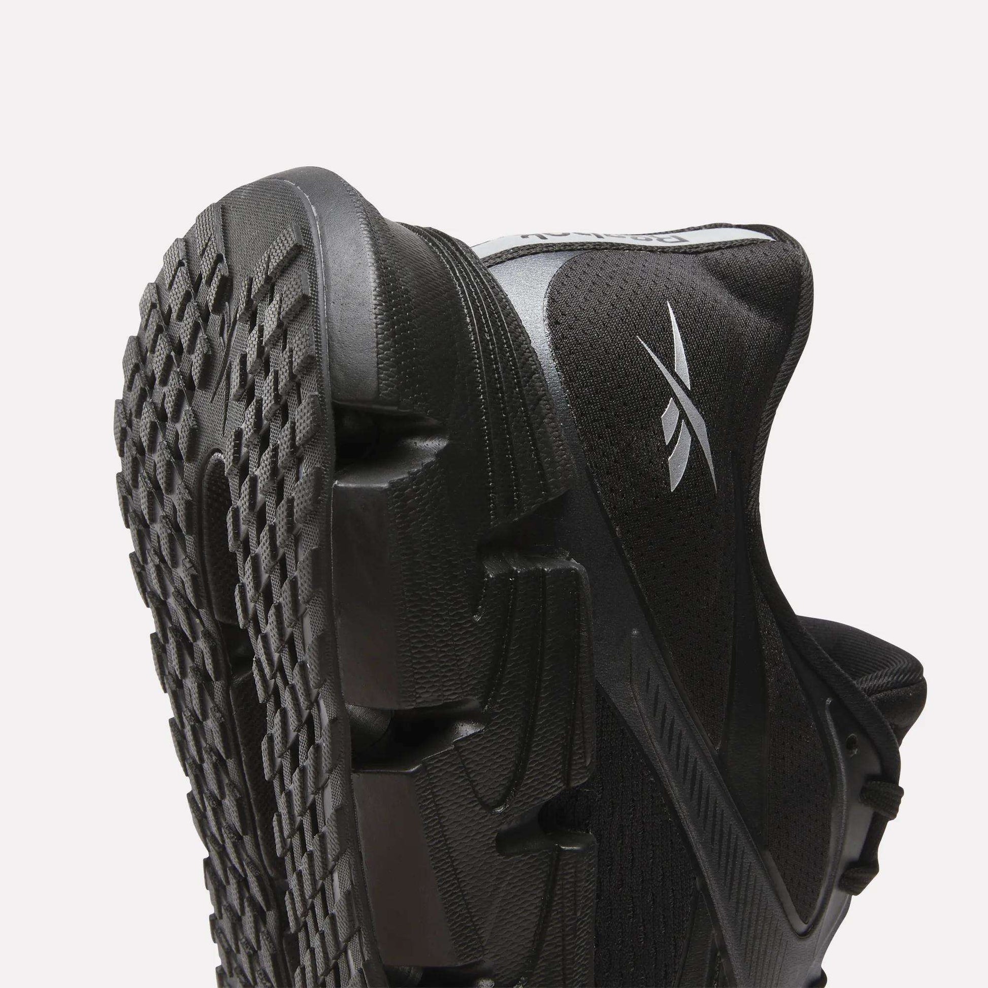 Close-up of Reebok Men's FloatZig 2 Running Shoes in black, featuring a textured rubber sole, energy-returning cushioning, and a white Reebok logo on the side, set against a plain light background.