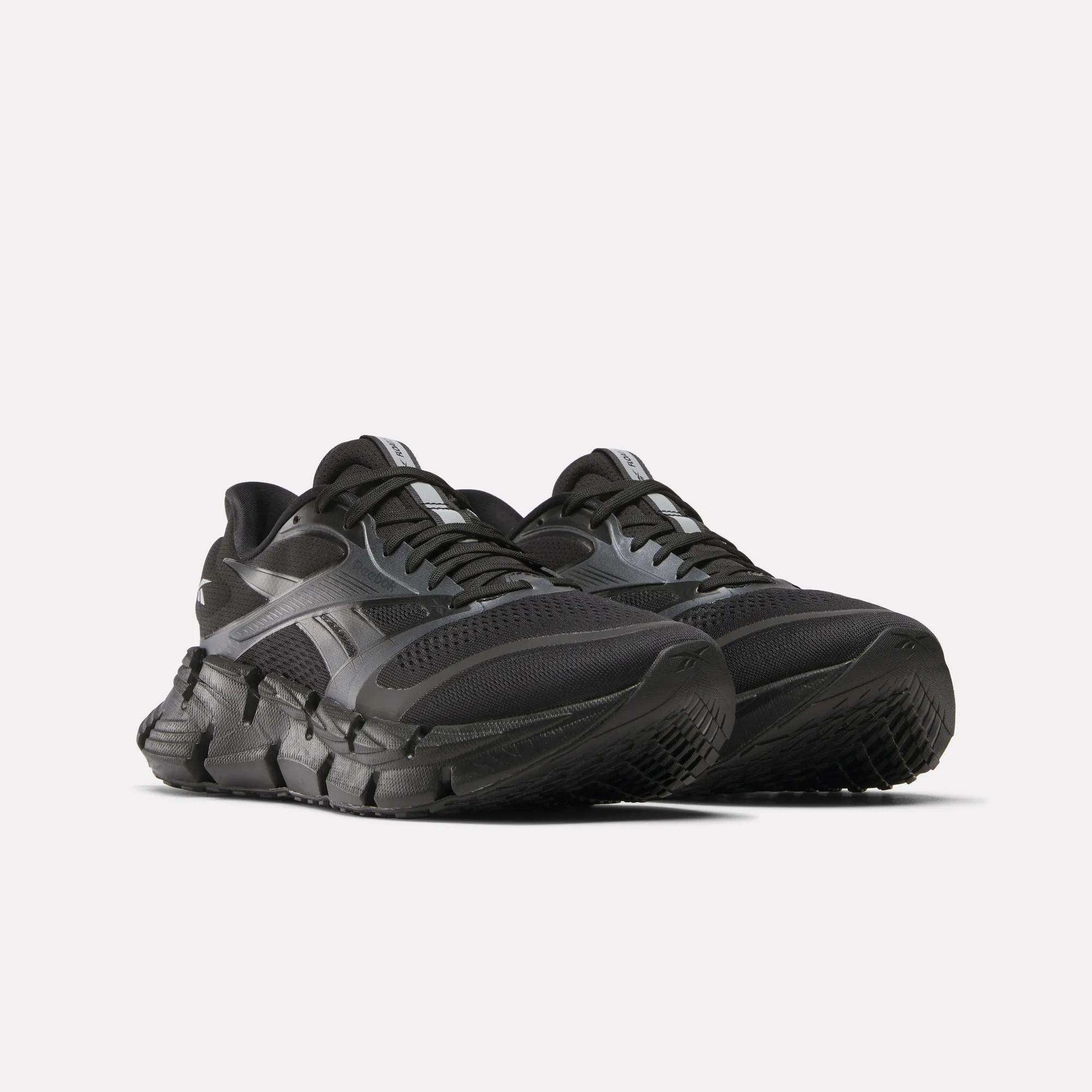 A pair of black Reebok Men's FloatZig 2 Running Shoes with thick, textured soles and mesh uppers, featuring energy-returning cushioning, are positioned side by side on a white background.